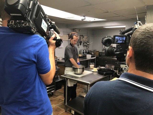 behind the scenes photo: chef does cooking demonstration while two camera operators record footage