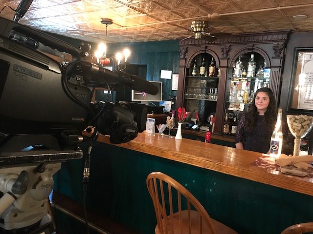 behind the scenes photo: guest stands behind bar while camera records footage